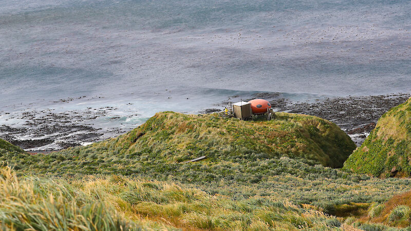 Small oval shaped orange hut overlooking bay