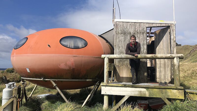 Scientist standing on porch of small oval orange hut