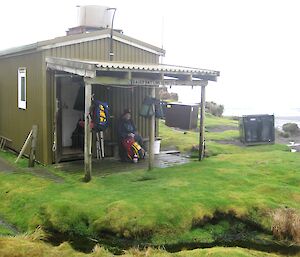 A man sits on the verandah outside a one-room wooden hut with a sign saying ‘Bauer Bay links motel'.