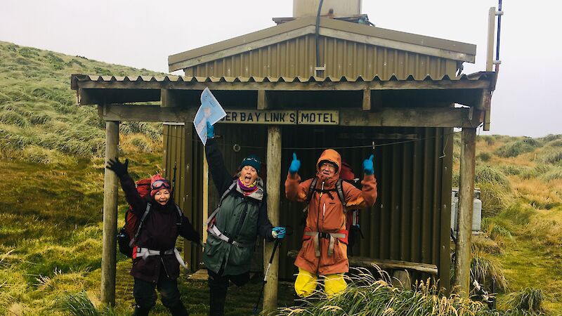 Three expeditioners outside the small wooden hut