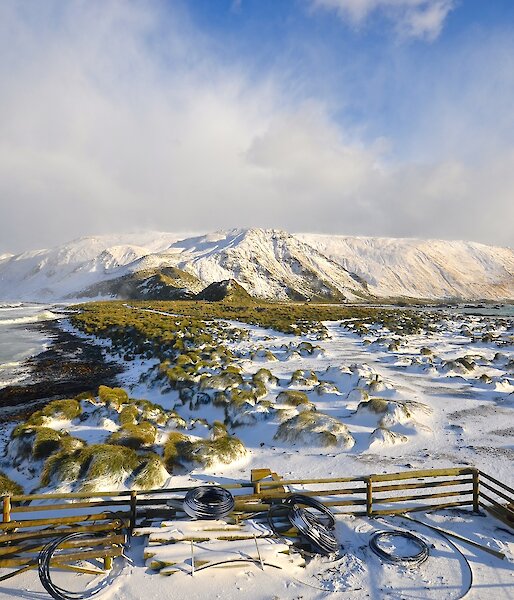 Looking south over the snow covered isthmus and the slopes up to the plateau. In the foreground is a timber fence enclosure to the fuel ‘farm’ including a store area for plastic polypipe and some fencing timber