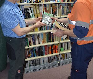 Two expeditioners consider a book in the Mawson library