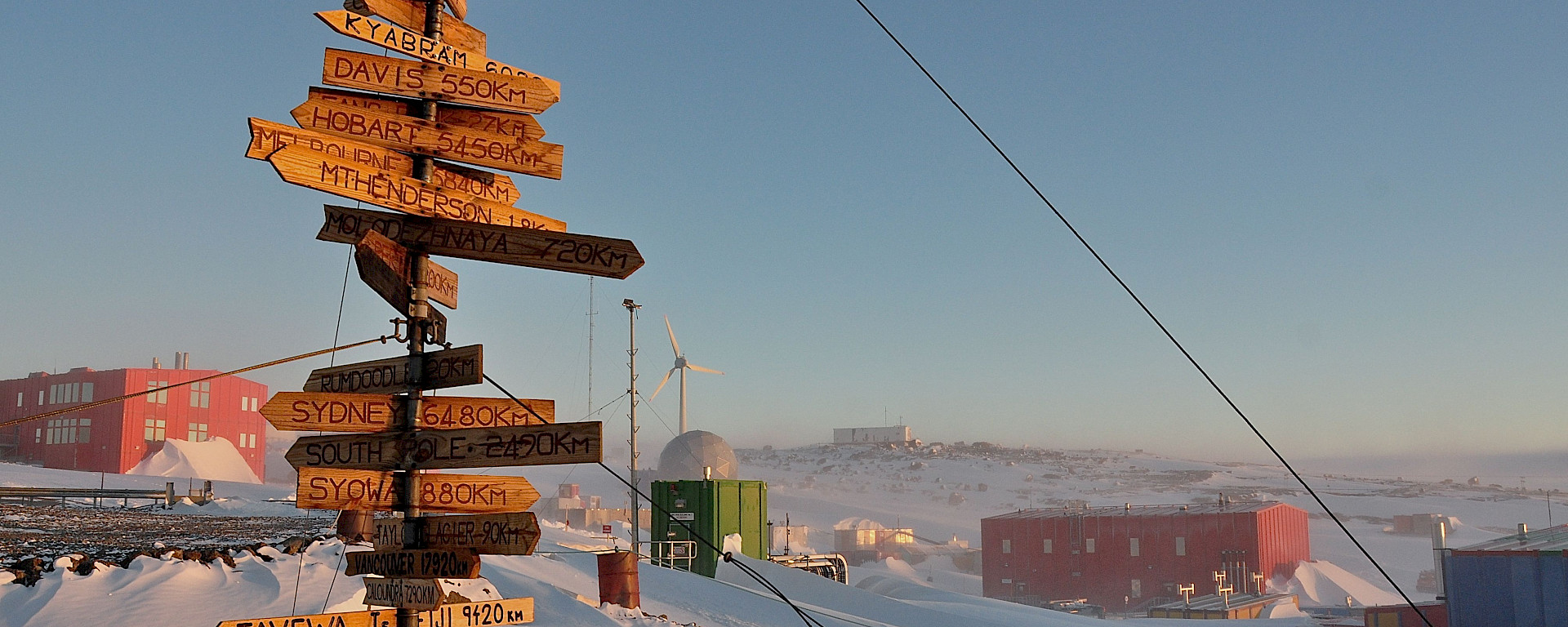 A tall wooden sign featuring many smaller plaques with town names pointing in the direction which they are located.