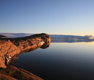 Sunlight makes the rocks glow golden, water lapping and wind turbines behind.