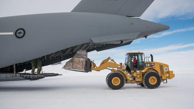 Large yellow tractor remove cargo at rear of heavy lift cargo aircraft.