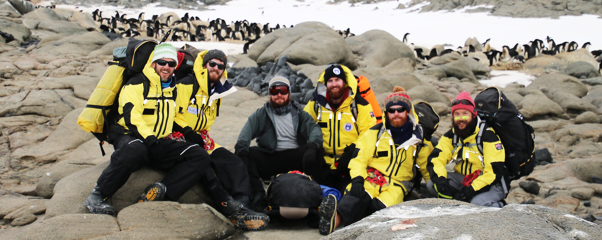 A group of expeditioners wearing yellow with penguins in background.