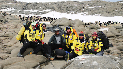 A group of expeditioners wearing yellow with penguins in background.