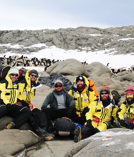 A group of expeditioners wearing yellow with penguins in background.