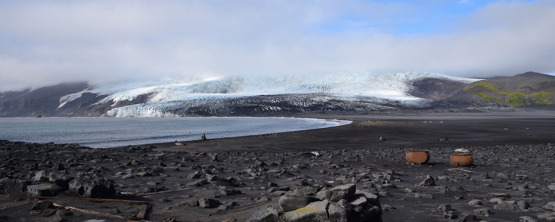 A black sand beach with elephant seals and two trypots, and ice-covered Stephenson Glacier in the background.