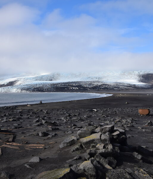 A black sand beach with elephant seals and two trypots, and ice-covered Stephenson Glacier in the background.