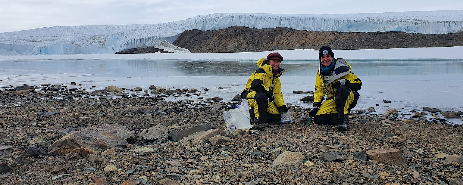 two scientists on rocky shore beside lake