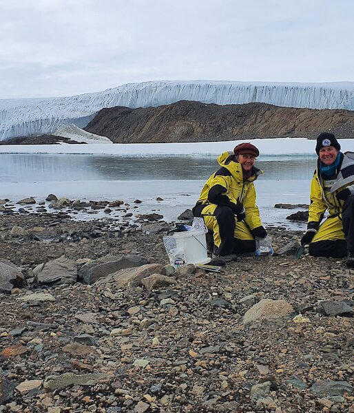 two scientists on rocky shore beside lake