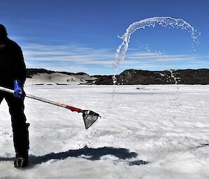 man flicks water out of ice hole with sieve