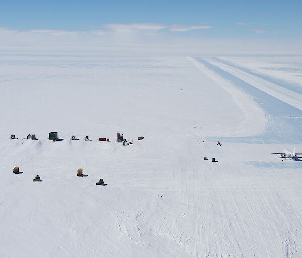 Aerial view of ice runway, buildings and large aircraft on ground in the expanse of the ice sheet