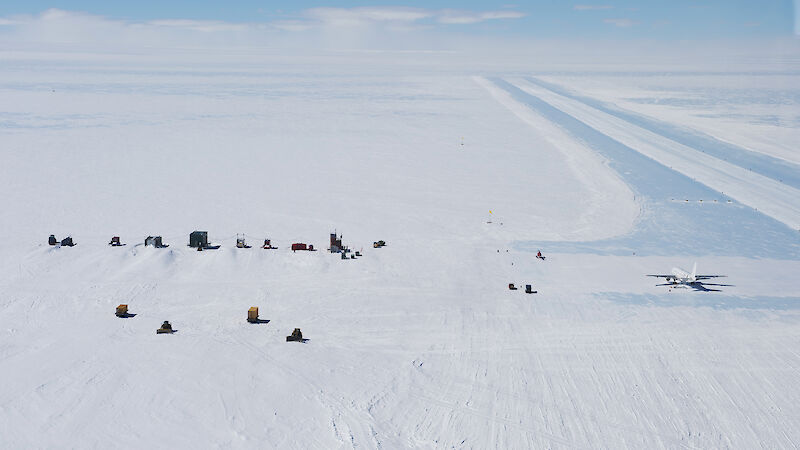 Aerial view of ice runway, buildings and large aircraft on ground in the expanse of the ice sheet