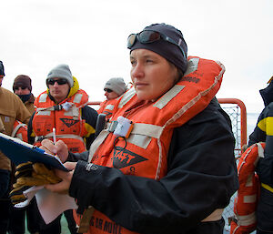 Deputy Voyage Leader with clipboard surrounded by expeditioners on the deck of ship