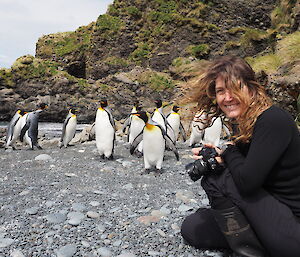woman approached by king penguins on rocky beach