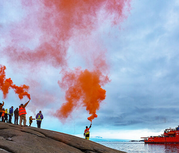 Expeditioners holding up flares to farewell the Aurora Australis icebreaker