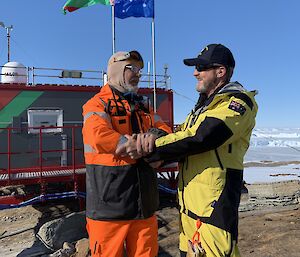 two men shake hands in front of brightly coloured building