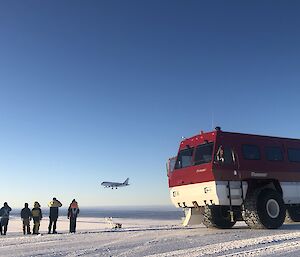 A group of people standing next to the bus, watching a plane land