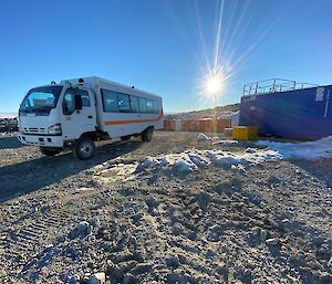 A passenger bus with the early morning sun above shipping containers