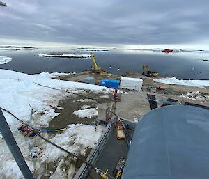 Looking down a hill partially covered with snow at fuel tanks, cranes, and shipping containers