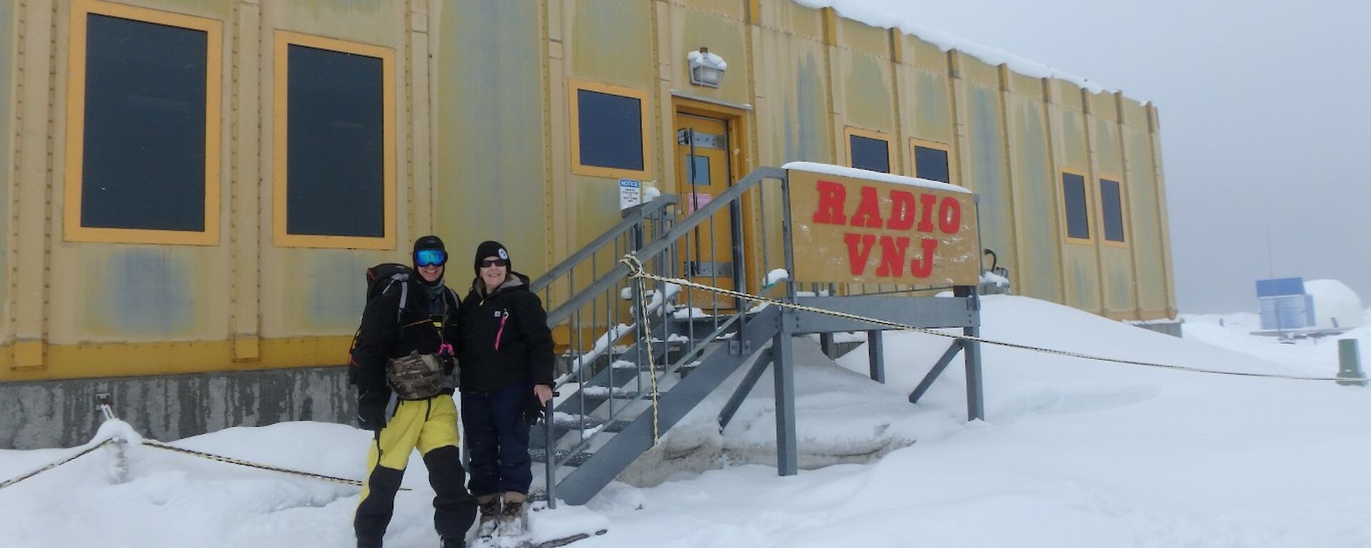 Two people in cold weather gear standing outside a building