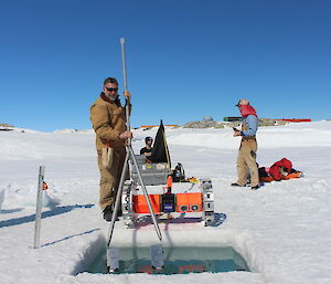 Four men on the ice standing around hole in the ice