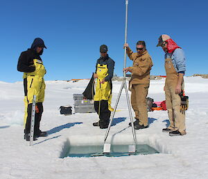 Four men looking into a hole in the ice