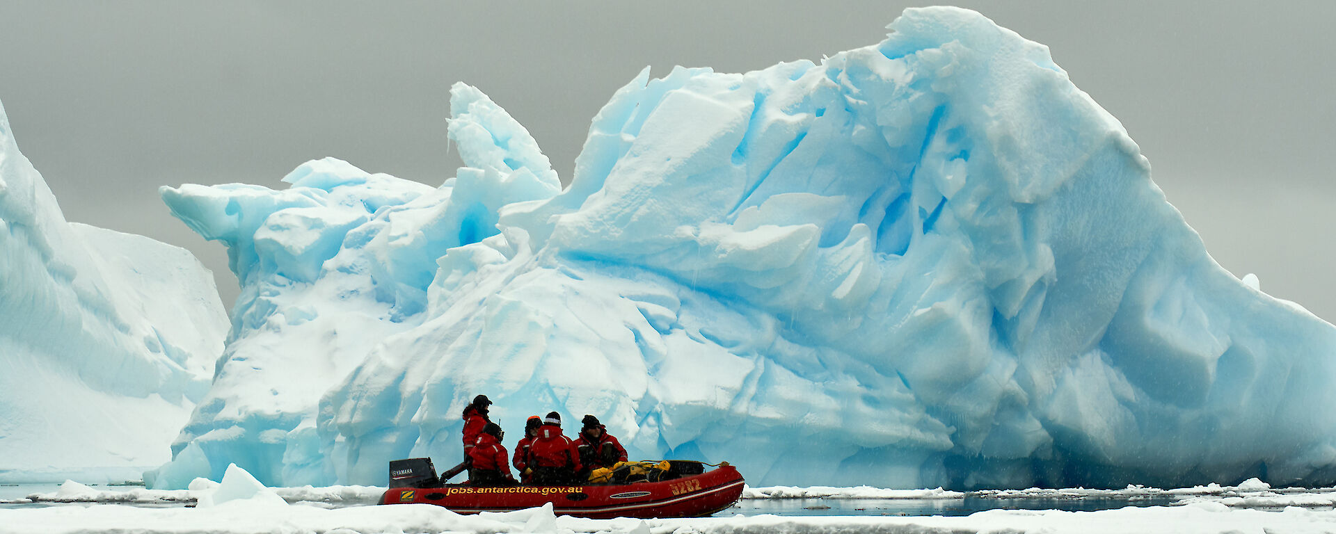 A small orange boat with an stunning iceberg backdrop.