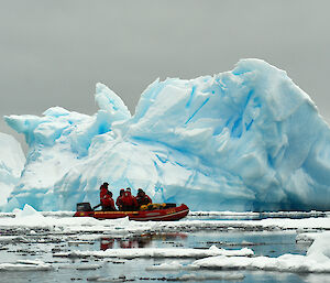 A small orange boat with an stunning iceberg backdrop.
