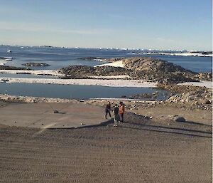 Three expeditioners stand next to the concrete helipad with a bamboo cane installed in the centre.