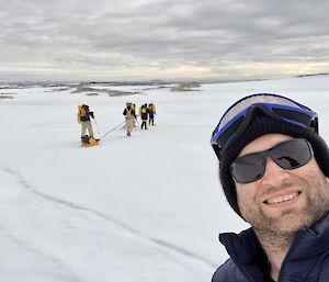 Self portrait of an expeditioner on the ice and four other expeditioners pulling sleds in the background