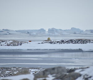 A rocky and snowy landscape with an old field hut in the distance