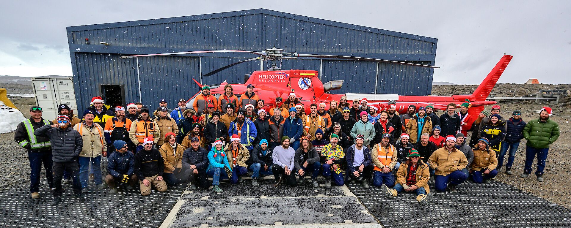 The Davis cohort pose in front of a red helicopter for a snowy, Christmas themed group photo.