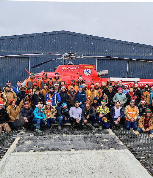 The Davis cohort pose in front of a red helicopter for a snowy, Christmas themed group photo.