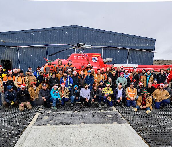 The Davis cohort pose in front of a red helicopter for a snowy, Christmas themed group photo.