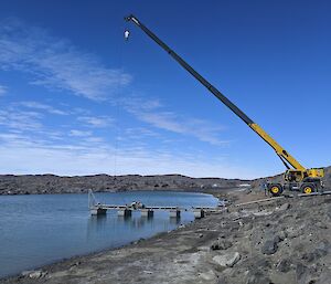 A large mobile crane holds a pontoon in place as it floats on the grey tarn.