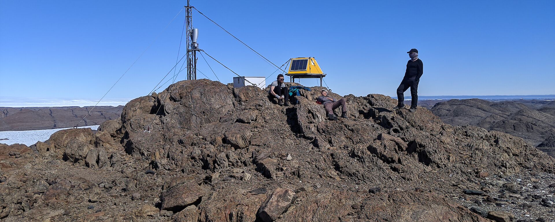 Three men sitting on rock summit