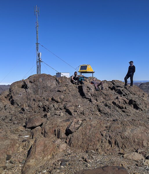 Three men sitting on rock summit