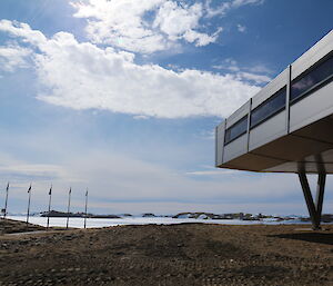 The sun beams through white clouds in a blue sky. The futuristic Bharati station occupies the right of frame while flagpoles are in the left.