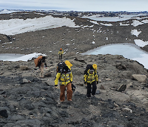 A survey team climbing up a hill at the brown, rocky, proposed aerodrome site