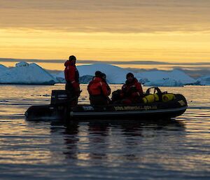 people in inflatable boat at sunset with icebergs