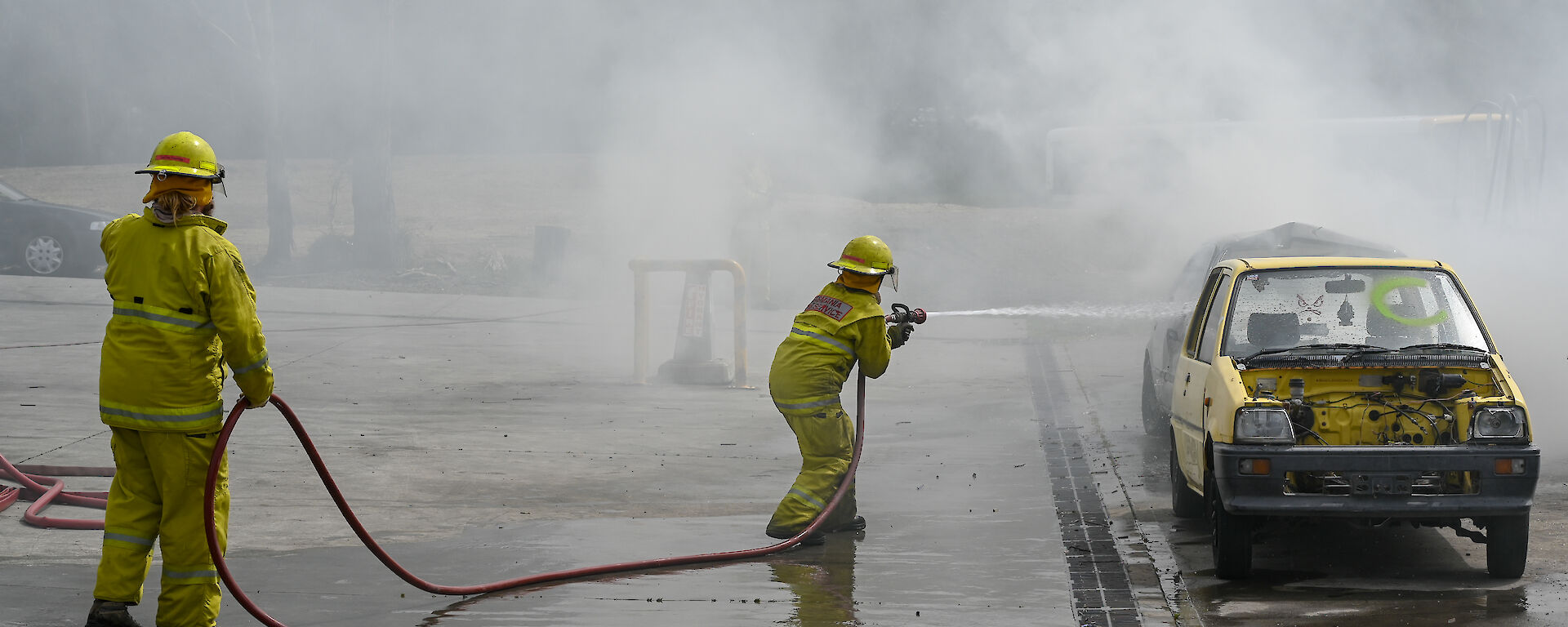 Chef Donna dressed in firefighting attire extinguishes a blazing car at fire training
