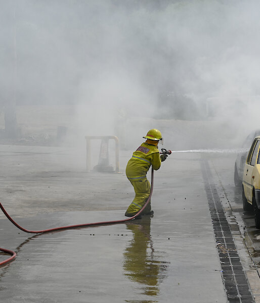 Chef Donna dressed in firefighting attire extinguishes a blazing car at fire training