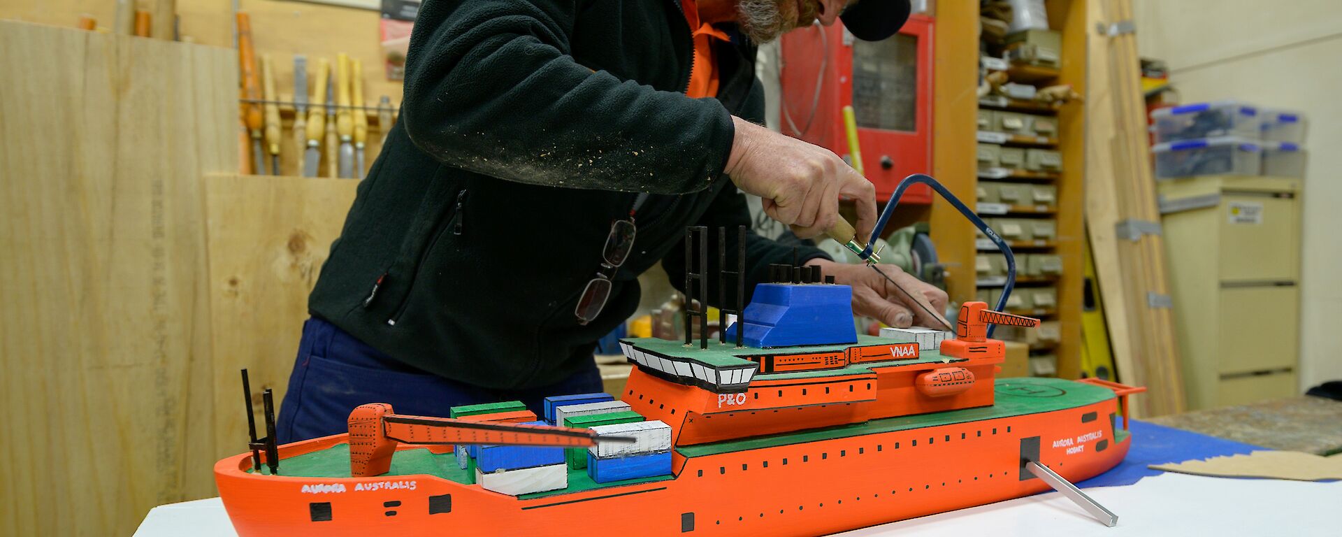 Carpenter makes a saw cut on his scale workshop model Aurora Australis ship