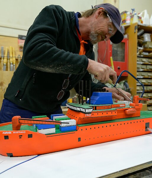 Carpenter makes a saw cut on his scale workshop model Aurora Australis ship