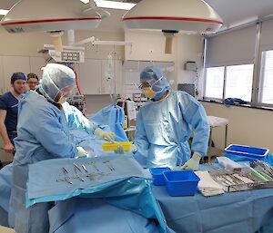 Doctor and assistant dressed in blue scrubs, work under the surgical theatre lights during a training scenario