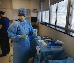 Lay surgical assistant in his surgical scrubs, gives two thumbs up as he counts the sterile medical equipment