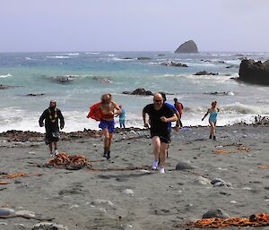 Swimmers emerge from the water and run up the beach